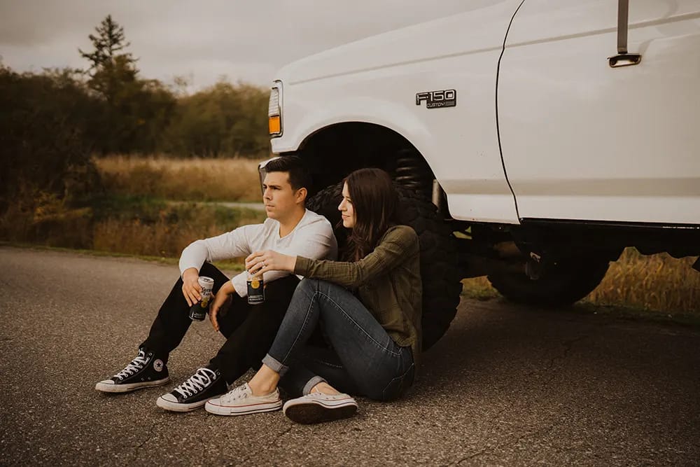 Couple drinking beer sitting against tire of truck