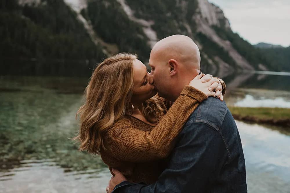 couple share a kiss with a mountain and clear waters in the backdrop