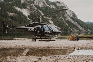 couple sitting beside helicopter with mountain in the background