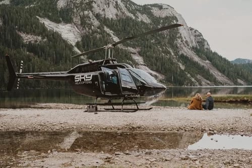 couple sitting next to a helicopter looking at a lake
