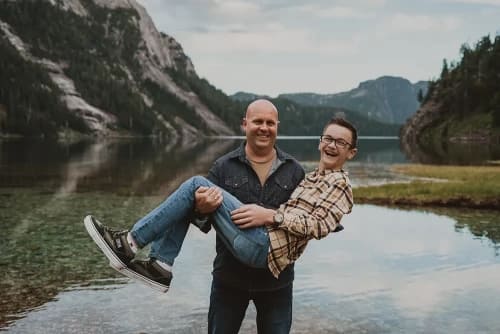 Dad carrying laughing son in front of a lake