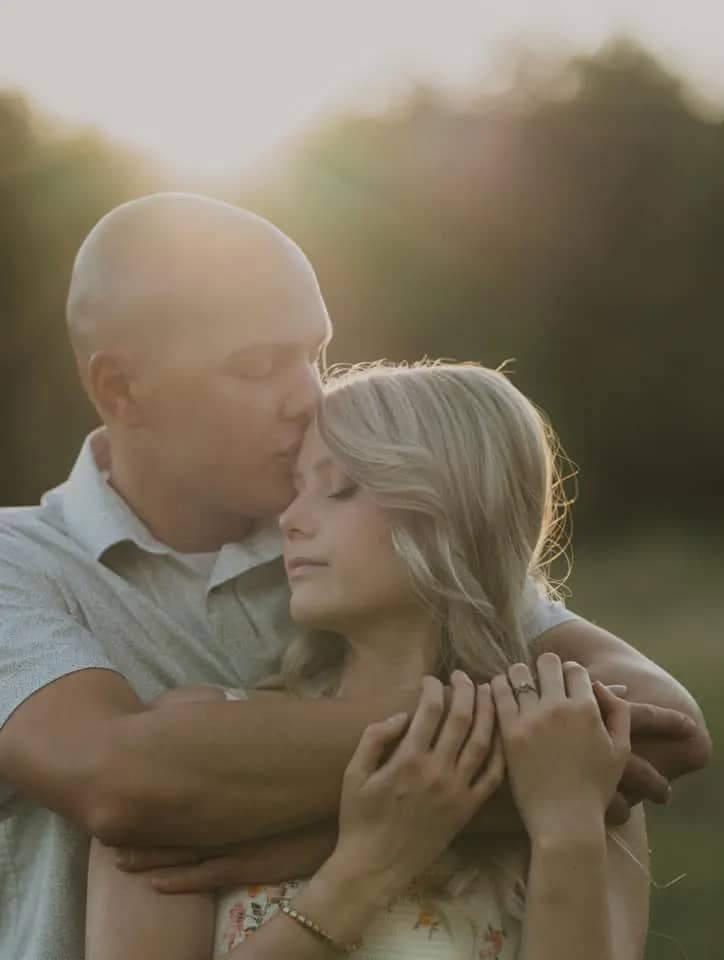 Man kissing his wife forehead with the sun shining on them